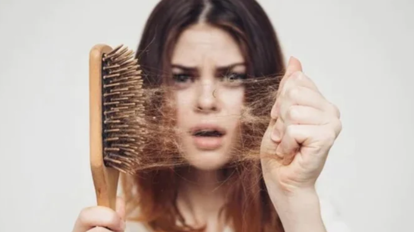 A woman pulls hair from her hair brush, shocked expression. Concept of thinning hair, hair loss, thinning hair solutions.