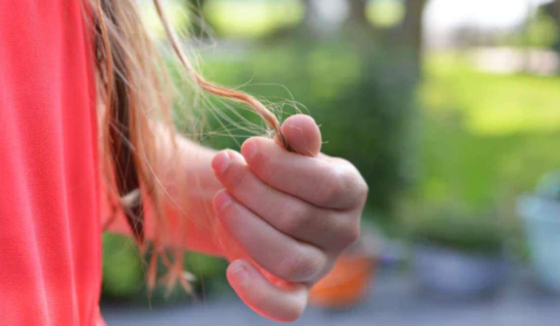 A woman with brown blonde thinning hair pulling at her hair. Concept of hair loss mistakes, hair mistakes to avoid for thinning hair. 